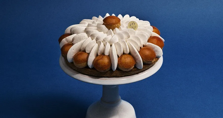 Dalloyau Saint-Honoré with caramelised choux and piped cream on a white cake stand against a deep blue background
